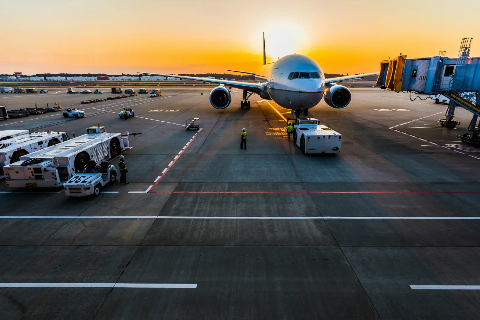 A cargo jet on an airport stand at sunset, with ground vehicles around it